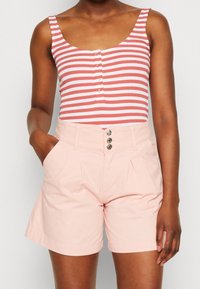 Bodysuit rayé rose et blanc, avec un col en scoop et des boutons décoratifs, associé à un short taille haute rose clair avec des plis à l'avant.