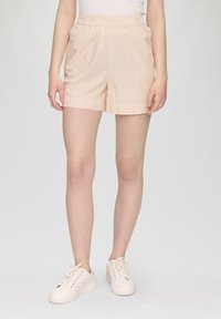 Helle rosa, gestreifte Shorts mit einem elastischen Bund. Aus weichem Material gefertigt. Kombiniert mit weißen Sportschuhen vor einem schlichten Hintergrund.