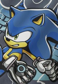 Blå karaktär med gula accenter, stora ögon och silverhandskar, framför en sprucken väggdesign med nyanser av grått och blått.