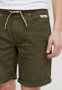 Olívazöld pamut rövidnadrág, húzózsinóros derékkal, felhajtott szegéllyel és elülső zsebekkel, kis szövetcímkével.