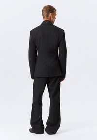 Svart pinstripe dress til med skreddersydd jakke og vide bukser. Stoffet er glatt, og designet har klassisk krage og strukturert skuldre.