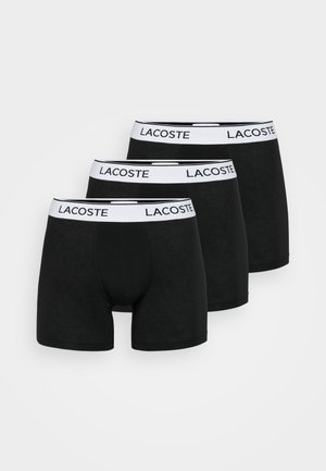 Schwarze Boxershorts im Dreierpack, mit einem weißen Bund, der das Lacoste-Logo trägt. Weicher Stoff mit enger Passform und ohne sichtbare Muster.