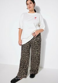 T-shirt bianca oversize con stampa "❤️ YOU" in rosso, abbinata a pantaloni ampi a stampa leopardo beige e scarpe slip-on nere.