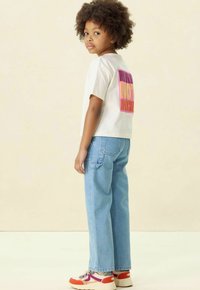 Witte grafische t-shirt met kleurrijke tekst op de achterkant, gecombineerd met lichtblauwe recht afgesneden jeans en meerkleurige sneakers.