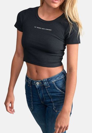 T-shirt noir côtelé court avec des manches courtes et le texte "LE TEMPS DES CERISES" sur le devant, associé à un jean bleu taille haute.