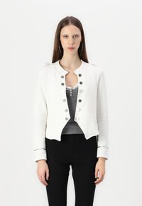 White cropped jacket with shoulder epaulettes, silver buttons, and a sleek design. Worn over a gray top and paired with black pants.