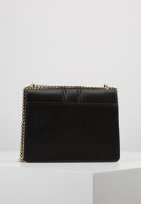 Borsa a mano in pelle nera con tracolla a catena, caratterizzata da una consistenza liscia, forma rettangolare e sottili dettagli cuciti sulla parte frontale.