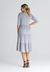 Szara sukienka warstwowa z rękawami do trzech ćwiartek, wykonana z miękkiego materiału. Projekt zawiera marszczony pas i zwiewną dolną część.