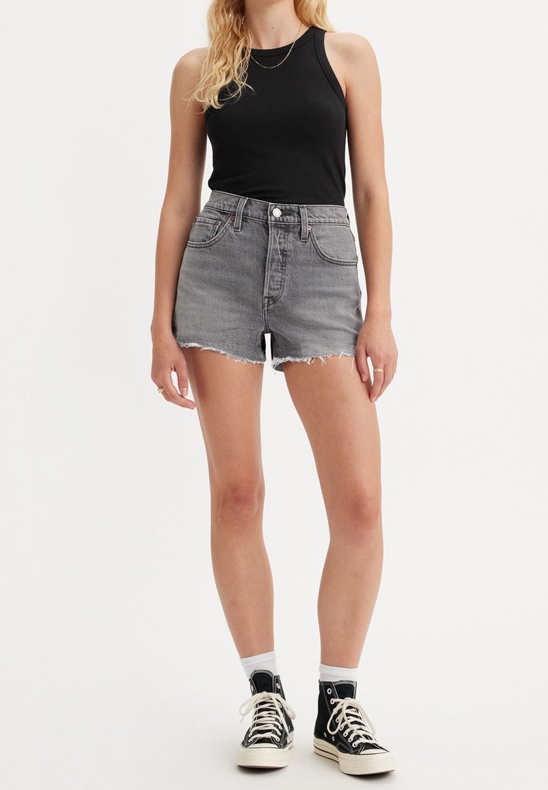 Shorts de mezclilla gris con dobladillo deshilachado, diseño de tiro alto, combinados con una camiseta sin mangas de canalé negra y zapatillas altas negras.
