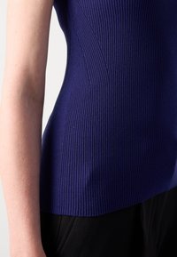 Ribbed, fitted top in deep purple, featuring vertical texture and side seam details. Paired with black fabric, highlighting contrast.