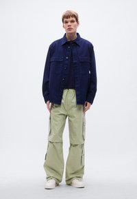 Υπερμεγέθη μπλε τζιν μπουφάν με δύο τσέπες στο στήθος, συνδυασμένο με ανοιχτοπράσινο παντελόνι cargo με πολλές πλαϊνές τσέπες. Άσπρα αθλητικά παπούτσια.