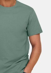 T-shirt manica corta di colore verde tenue, realizzata in cotone, con collo rotondo e una texture liscia, dallo stile morbido.