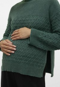 Zielony sweter z dzianiny z fakturowanym wzorem diamentowym, wysokim kołnierzem, ściągaczami na krawędziach i rozcięciami po bokach. Miękki materiał, luźny krój.