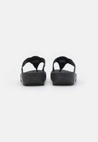 Black sandals with adjustable straps, flat soles, and textured footbeds. Rear view shows minimalist design and lack of prominent adornments.