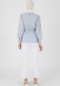 Vaaleansininen pusero, jossa on puffattuja hihoja, taitettu vyötärö ja nappikoristeet. Yhdistetty valkoisiin suoriin housuihin ja sandaaleihin.