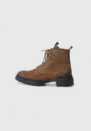 Brown suede ankle boots with black rubber sole and laces, featuring metal eyelets and a pull tab on the back for easy wear.
