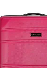 Hard-shell pink suitcase with a textured surface, black handle, subtle horizontal lines, and a small black logo plate.
