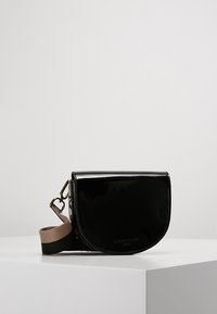 Černá lakovaná crossbody taška zaobleného tvaru, s klopovým uzávěrem a kontrastním béžovým popruhem s černým akcentem.