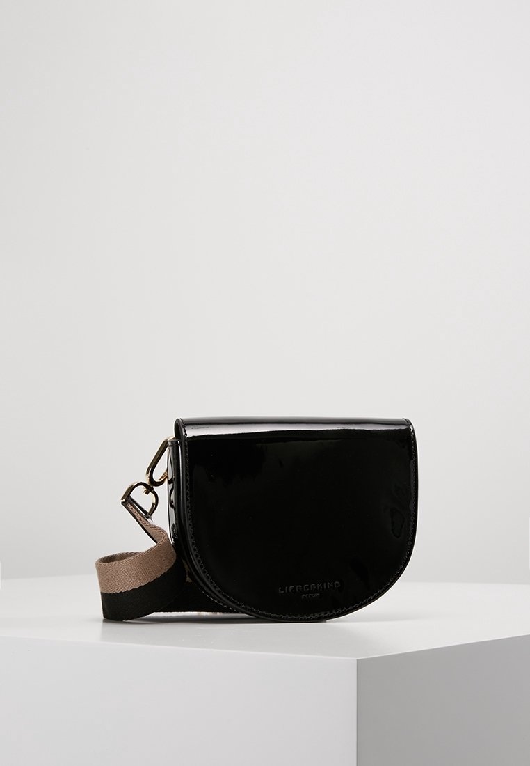 Černá lakovaná crossbody taška zaobleného tvaru, s klopovým uzávěrem a kontrastním béžovým popruhem s černým akcentem.