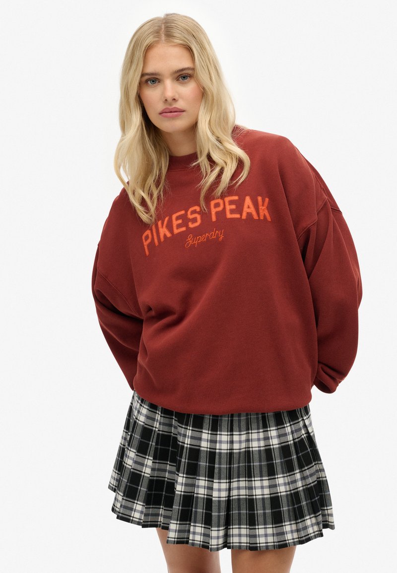 Sudadera oversized burdeos con bordado en naranja de "Pikes Peak". Combinada con una falda de tablas en blanco y negro.