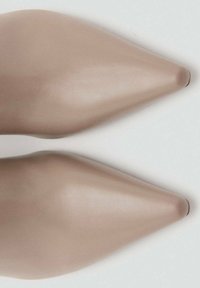 Escarpins beiges à bout pointu en cuir lisse, présentant un design épuré et des coutures discrètes le long des bords. Pas de matériel visible.