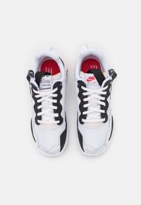 Scarpe sportive bianche e nere in mesh e materiali sintetici, con collarino imbottito e lacci visibili. Accenti rossi sulla soletta interna.