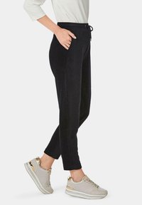 Zachte zwart stoffen joggers met een elastische tailleband en zijzakken, gecombineerd met lichtgrijze sneakers met gouden accenten.