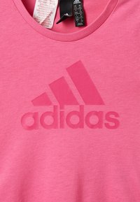  camiseta de algodón rosa con un gran logo de Adidas mate y en sombra en el centro, con cuello redondo y mangas cortas.