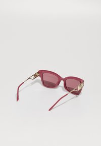Rammeløse firkantede solbriller med dype rosa linser, dristige rosa plastinnramminger og gullfargede metallakenter ved templene.