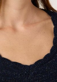 Mörkblå stickad tröja med en scallop-designad halsringning och subtil metalltråd. Texturen ser mjuk ut med en ribbad design.