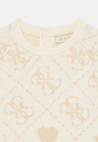 Cremefarbener Pullover mit gewebtem Rautenmuster und goldenen Akzenten, Rundhalsausschnitt und gerippten Abschlüssen. Markenetikett ist innen sichtbar.