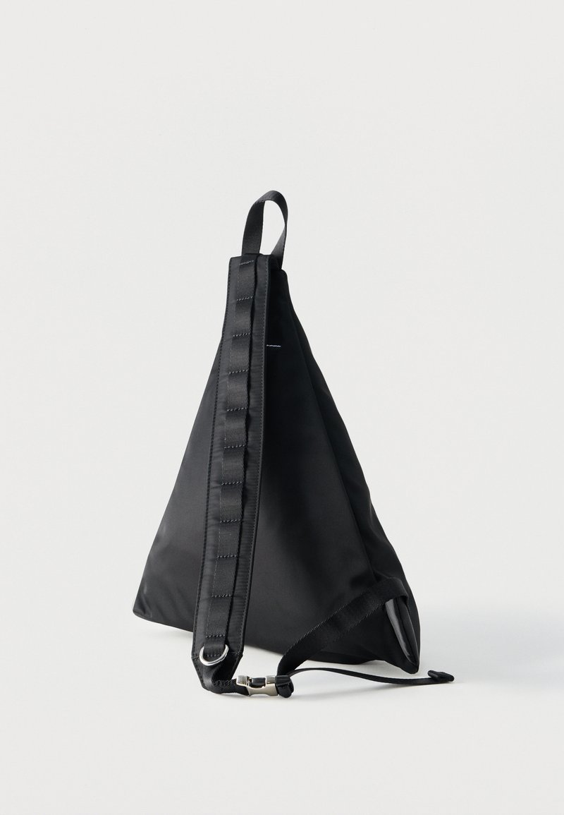 Sac à dos bandoulière triangulaire noir avec sangle ajustable rembourrée et boucle métallique sur fond blanc.