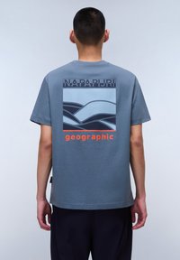 Gray short-sleeve t-shirt featuring a blue graphic of wavy lines and "NAPAPURJI" text above "geographic" in orange at the back.
