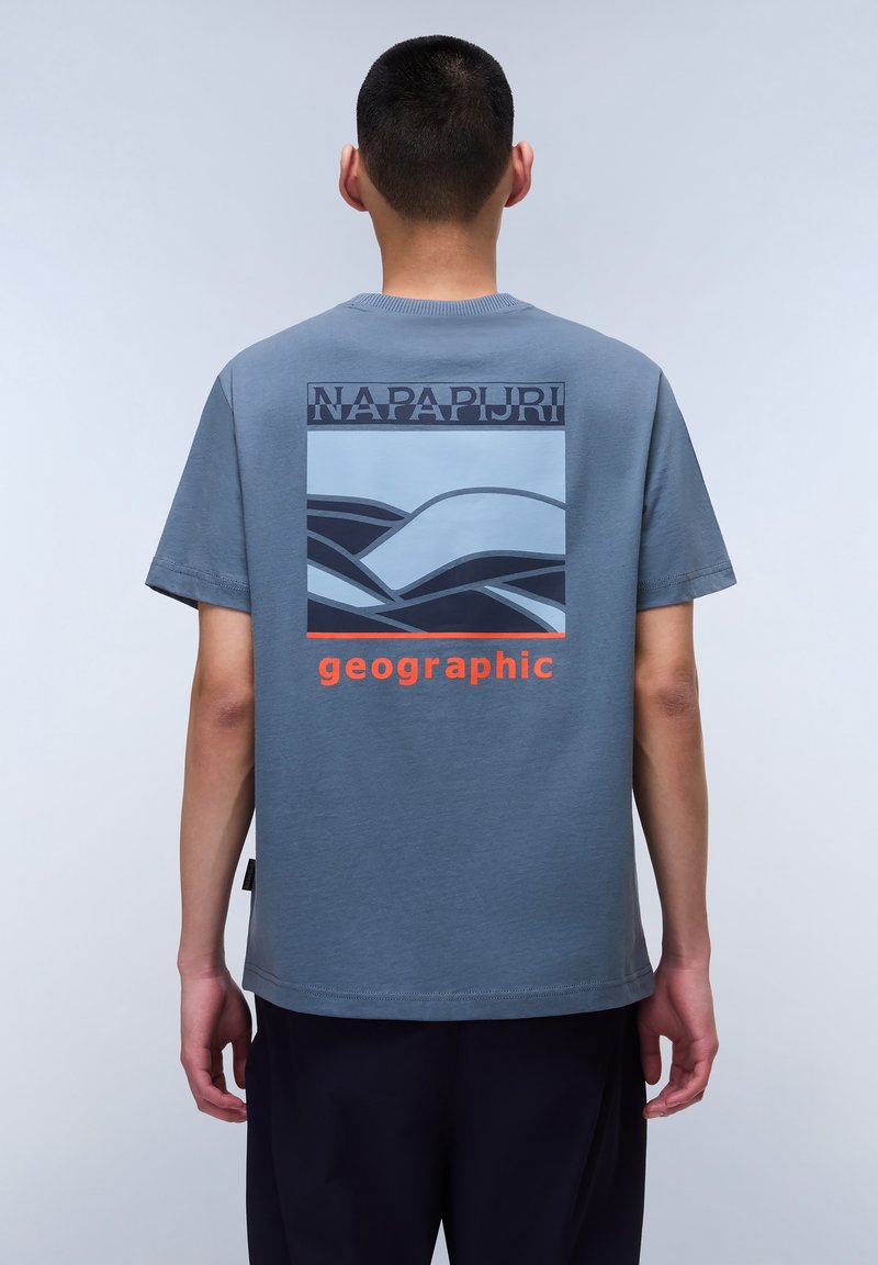 Gray short-sleeve t-shirt featuring a blue graphic of wavy lines and "NAPAPURJI" text above "geographic" in orange at the back.