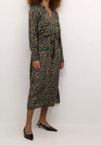 Abito lungo con stampa leopardata in verde spento e nero, con chiusura a bottoni davanti, vita legata e maniche lunghe. Abbinato a scarpe slingback nere.