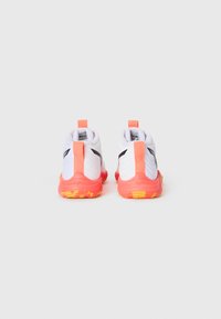 Pair of white athletic shoes with coral pull tabs and soles, black logo on sides, viewed from the back on a plain light background.