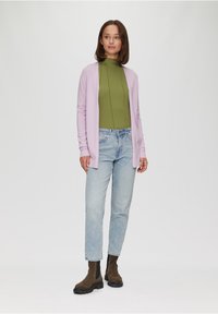 Cardigan violet clair sur un top vert, avec un jean bleu clair et des bottines brunes. Texture lisse, coupe décontractée et manches longues.