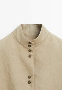 Beige liinakraega särk viie tumeda nupuga, millel on kumer disain ja peene tekstuur. Ülemine nupp asub krae peal.