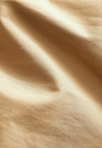 Tessuto beige chiaro con una consistenza liscia, leggermente stropicciato, che mostra trame sottili e un colore uniforme in tutto il tessuto, adatto a diverse applicazioni.