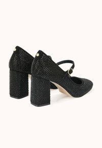 Chaussures à talons noirs avec une texture cloutée, un bout arrondi et une bride à la cheville. Dotées d'un talon épais et d'accents brillants à l'arrière.