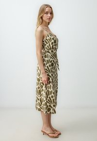 Beige midi-jurk met bloemenprint en donkergroene abstracte patronen, voorzien van dunne schouderbanden en een gestrikt taille-detail.