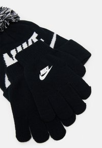 Bonnet en tricot noir avec un logo "NIKE" blanc et un pompon; gants noirs assortis avec un logo Nike blanc, tissu texturé, ajustement serré.