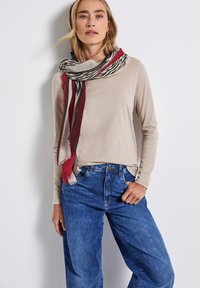 Beige langemouwen top gecombineerd met blauwe wijde jeans. Een multicolore sjaal met rode, grijze en crèmekleurige strepen en een zebra print detail.