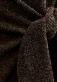 Brązowa tkanina o strukturalnej powierzchni, z miękkim, puszystym wykończeniem i detalem w formie supła. Materiał wydaje się gruby i ciepły, o bogatym, jednolitym kolorze.