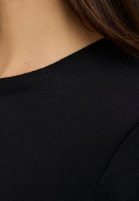 Schwarzer gestrickter Pullover mit rundem Ausschnitt und geripptem Muster, der eine Nahaufnahme des Schulterbereichs und des Stoffdetails zeigt.
