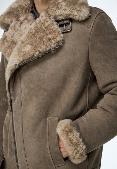 Bruine suède jas met een grote, gestructureerde nepbontkraag en manchetten, ritssluiting en zijzakken. Geaccentueerd met een metalen gesp.