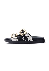 Slide sandals with black and white cow print upper, two gold-tone buckles, and a textured black sole.