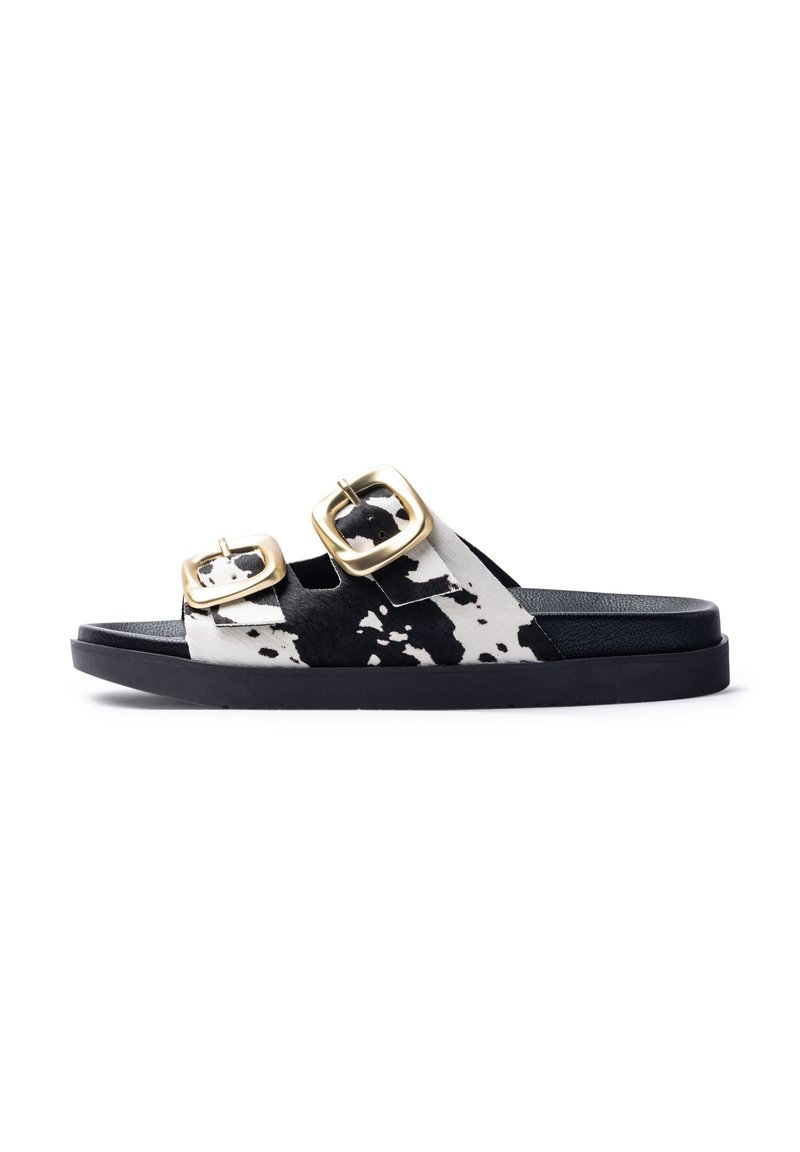 Slide sandals with black and white cow print upper, two gold-tone buckles, and a textured black sole.