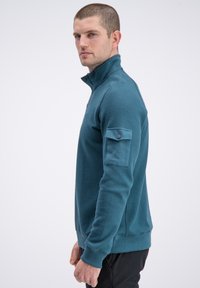 Bluza z suwakiem w kolorze morskim, z teksturowanymi panelami na rękawach, ściągaczami na mankietach oraz zapinanym na suwak kieszonką na piersi do użytku praktycznego.