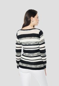 Fekete, fehér és szürke csíkos pulóver. Laza szabású, hosszú ujjú, texturált kötött mintával és nyitott szövésű díszítésekkel.